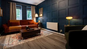 A living room with a dark blue wall, a red sofa, a wooden coffee table, and two floor lamps. - Finnieston 1BR | Walk to Hydro & SEC | Parking (Glasgow)