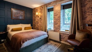 A bedroom with a bed, a chair, a window with curtains, and a wall-mounted lamp. - Finnieston 1BR | Walk to Hydro & SEC | Parking (Glasgow)