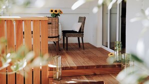 Une terrasse en bois avec une chaise en osier et une petite table, un vase rempli de tournesols et un porte-bougie en verre.