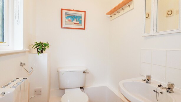A bathroom with a toilet, a sink, a mirror, and a framed picture on the wall. - Acorns (Falmouth)
