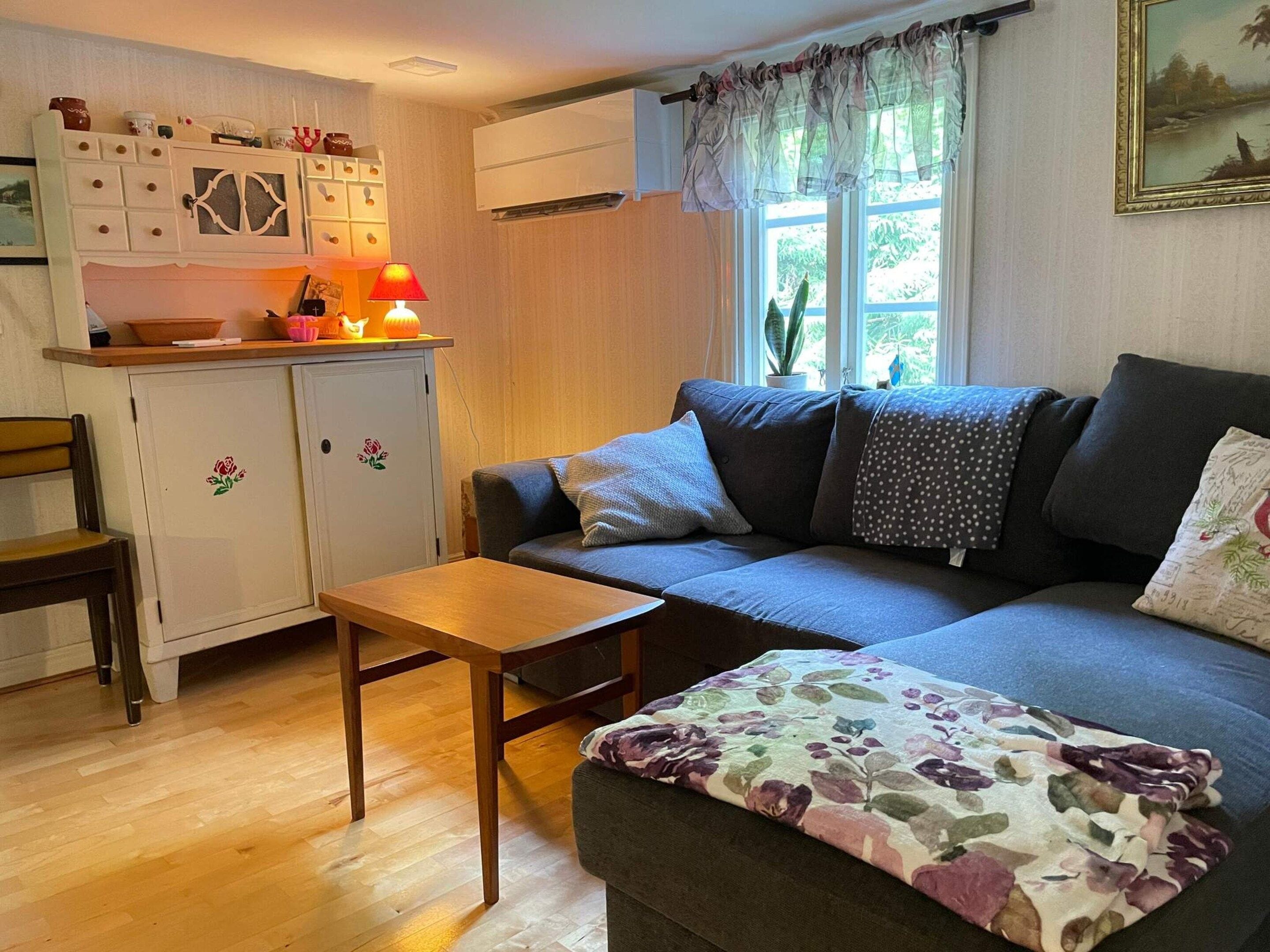 Uma sala de estar aconchegante com um sofá, uma mesinha e um armário com objetos decorativos.