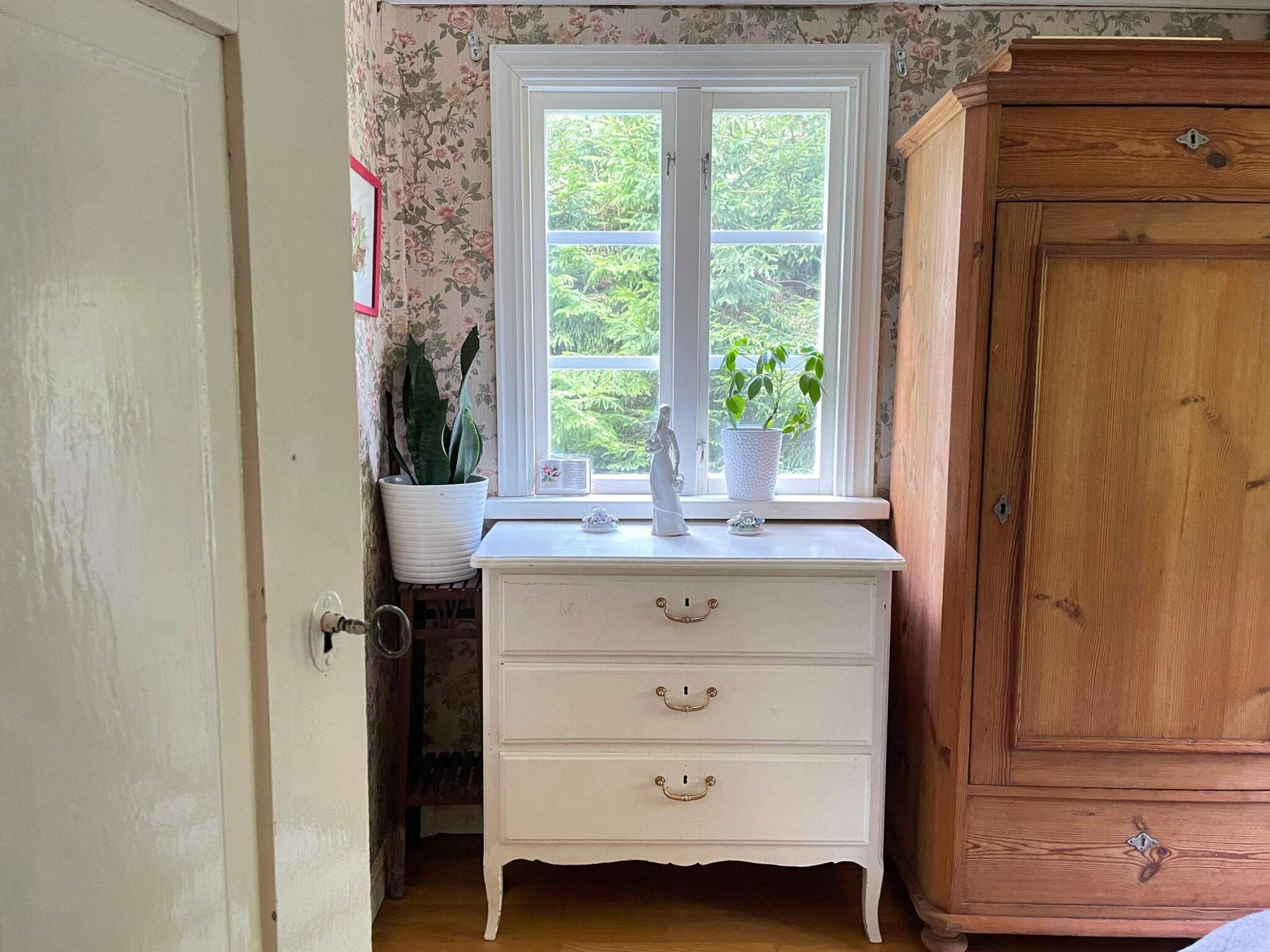 A room with a white dresser, a wooden cabinet, and a window with a view of greenery.