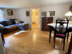 A living room with a sofa, a wooden bench, a dining table with a chair, a cabinet, and a lamp.