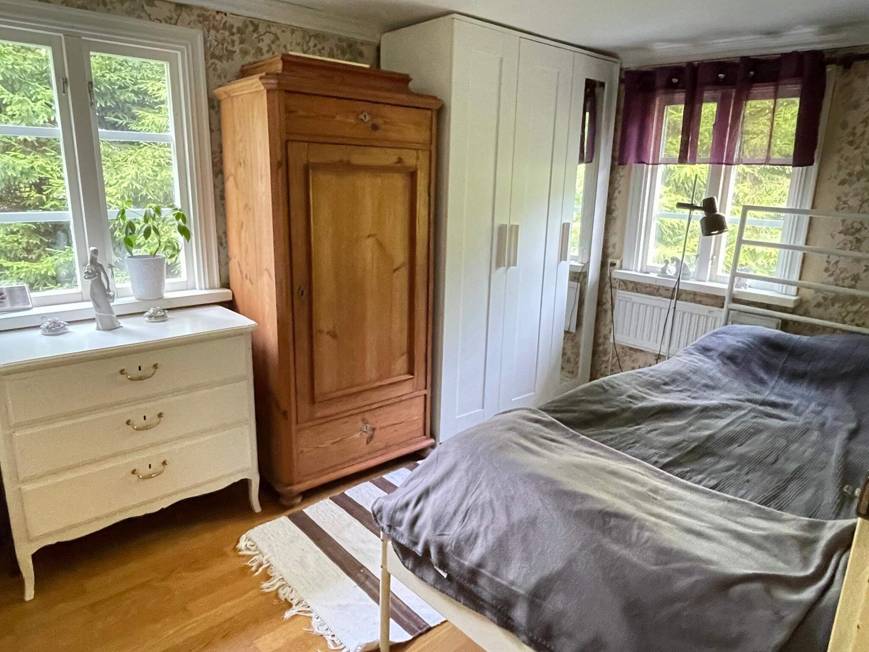 Een slaapkamer met een bed, een dressoir, een kledingkast en een raam met gordijnen.