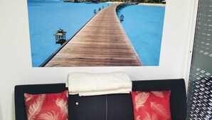 A black sofa with red and white patterned pillows, a white throw blanket, and a large tropical beach scene poster on the wall. - SEA HOUSE Madeira (Funchal)