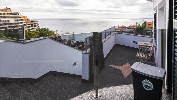 A balcony with a star-shaped tile, a trash bin, and a view of the sea and buildings. - SEA HOUSE Madeira (Funchal)