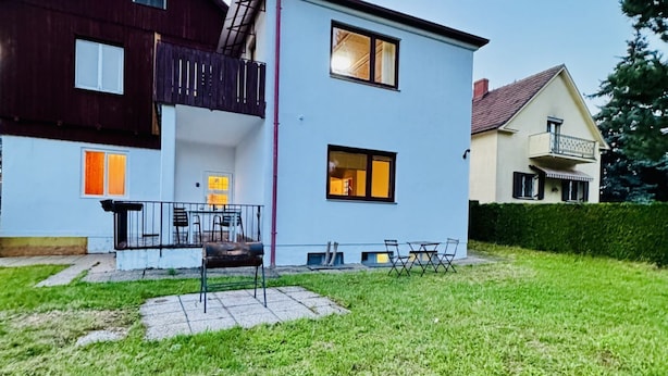 Une maison à deux étages dotée d’un balcon, d’une terrasse avec des chaises et d’une pelouse bien entretenue.