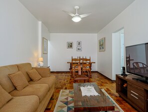A living room with a sofa, a dining table with chairs, a ceiling fan, and a television. - Apto a 700m da Praia do Leblon com Wi-fi e ar (Rio de Janeiro)