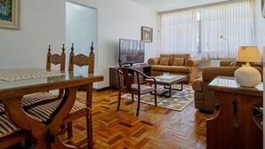 A living room with a wooden dining table, chairs, a sofa, a television, and a ceiling fan. - Apto a 700m da Praia do Leblon com Wi-fi e ar (Rio de Janeiro)