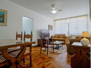 A living room with a wooden dining table, chairs, a sofa, a television, and a ceiling fan. - Apto a 700m da Praia do Leblon com Wi-fi e ar (Rio de Janeiro)