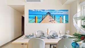 A dining area with a wooden table set for four, a painting of a beach scene, and a Christmas tree with ornaments. - All Inclusive VIP Celeb 5 Star Resort Pool Spa Gym (Parañaque)