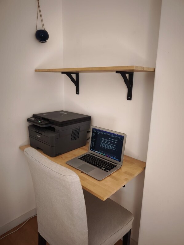 Un espace de travail avec un ordinateur portable sur un bureau en bois, une imprimante et une chaise.