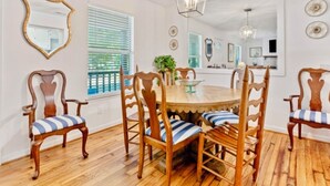 Un espace repas avec une table ronde en bois entourée de six chaises dotées de coussins à rayures, un plancher en bois et un luminaire suspendu au plafond.