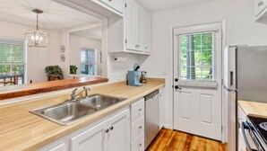 Une cuisine moderne avec des meubles blancs, un plan de travail en bois, un évier en acier inoxydable et un réfrigérateur.
