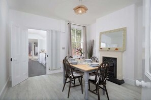 Une salle à manger avec une table en bois dressée pour quatre personnes, une cheminée et un grand miroir au mur.