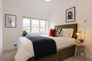 Een slaapkamer met een bed, een raam, een bedlamp en kunst aan de muren.