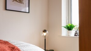 A bedroom with a bed, a bedside lamp, a framed picture, a window with a plant, and a small table with a bowl. - Spacious Home | Driveway Parking | Minutes from M1 (Nottingham)