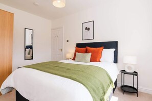 A neatly arranged bedroom with a bed, pillows, a bedside table, and a mirror. - Spacious Home | Driveway Parking | Minutes from M1 (Nottingham)