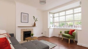 A living room with a fireplace, a sofa, a green armchair, and a large window. - Spacious Home | Driveway Parking | Minutes from M1 (Nottingham)