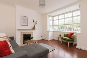 Un salon avec une cheminée, un canapé, un fauteuil vert et une grande fenêtre.