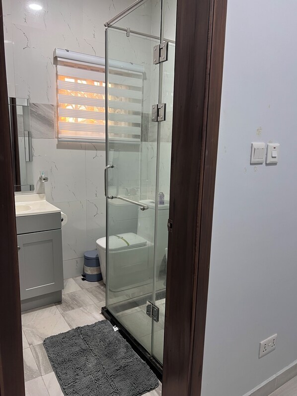 Un baño con cabina de ducha de vidrio, inodoro, lavabo y espejo.