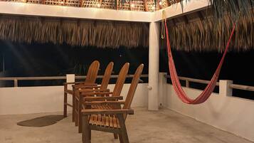 A thatched-roof outdoor seating area with wooden chairs and a red hammock.