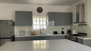 Une cuisine moderne avec des meubles gris, un grand îlot central, des appareils en acier inoxydable et une horloge au mur.