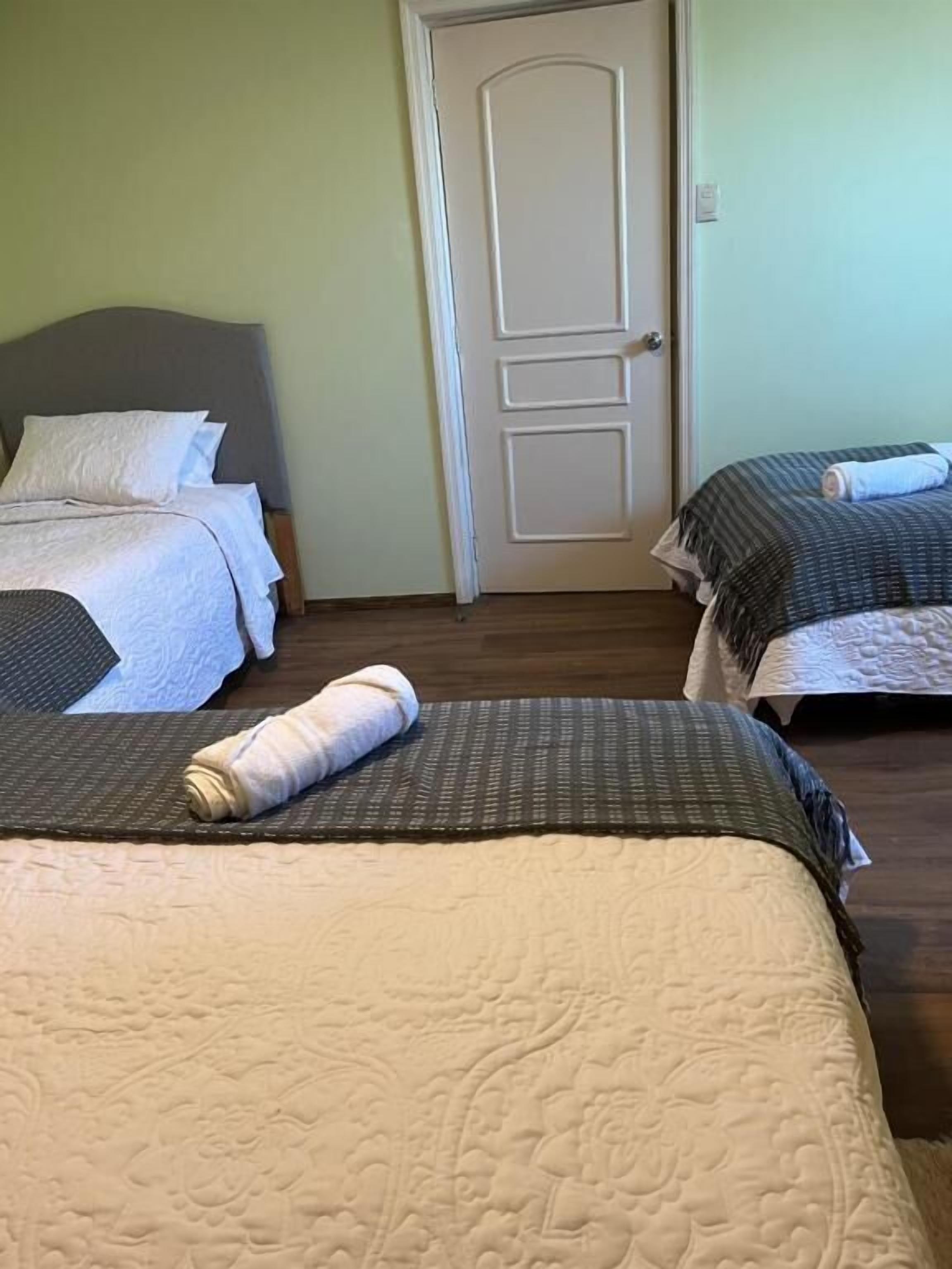 Habitación de hotel con tres camas, cada una con un estilo de ropa de cama diferente. Hay una puerta en el centro de la habitación.