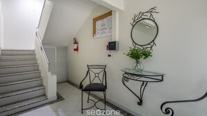Un escalier avec une rampe, un miroir fixé au mur, une petite table avec un vase de fleurs et un tableau d’affichage avec des papiers.