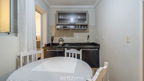 Une cuisine compacte avec un coin repas, comprenant une table recouverte d’une nappe à motifs, une chaise et un four encastré.
