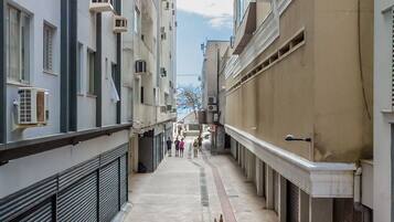 A narrow urban alleyway with buildings on either side, featuring air conditioning units, a visible staircase, and a pedestrian walkway.