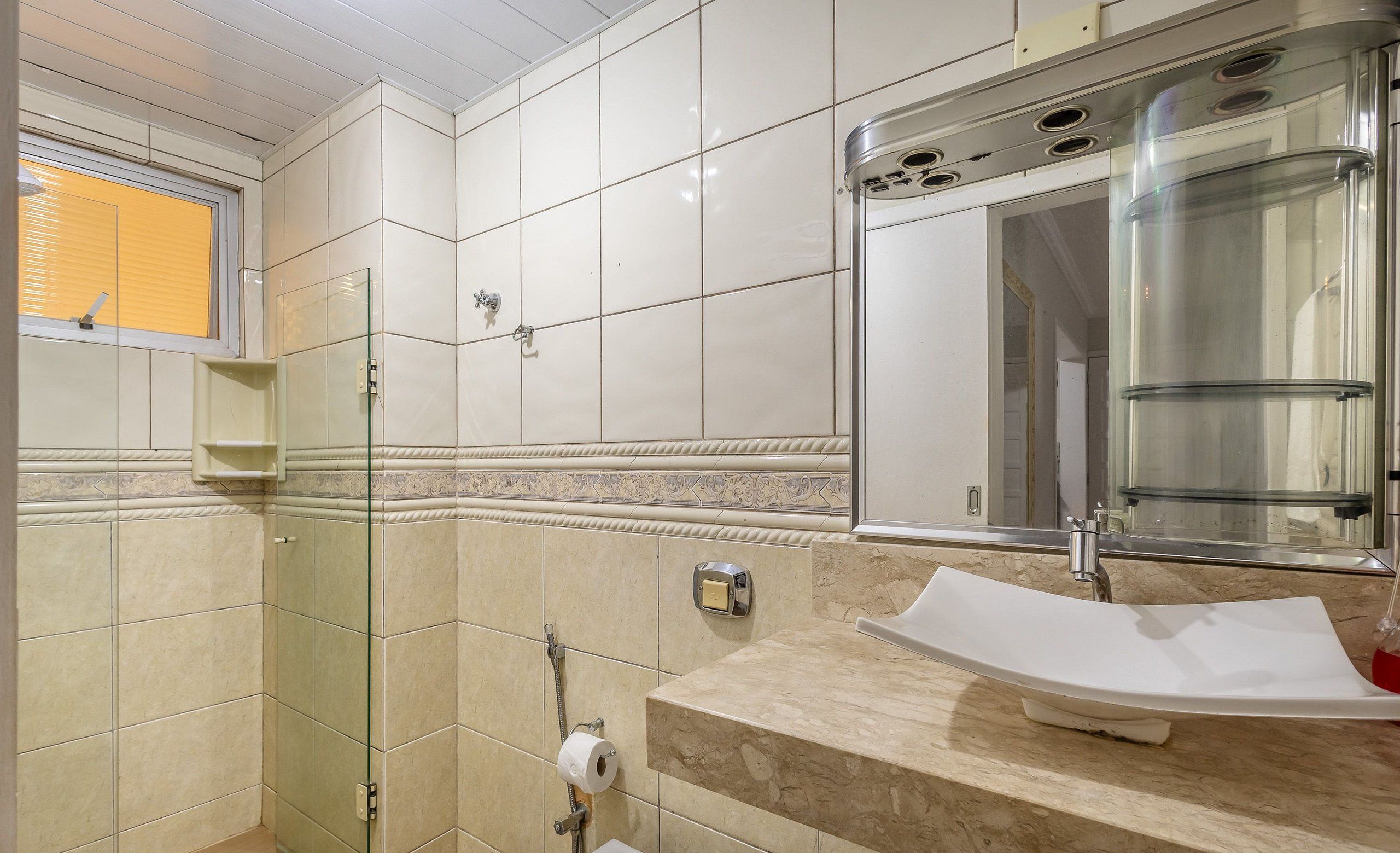 A bathroom with a glass shower enclosure, a sink with a marble countertop, and a mirror above the sink.