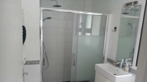 Un baño moderno con ducha envuelta en vidrio, baldosas blancas y un lavamanos blanco con un espejo encima.