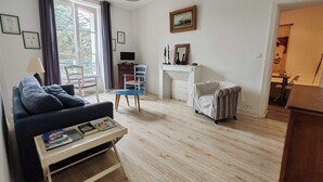 A living room with a sofa, a small table with books, a blue chair, a fireplace, and a painting on the wall. - Bright apartment with private beach access (Saint-Lunaire)