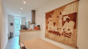 A modern kitchen with a wooden table, a large tapestry, and a view of the outdoors. - Bright apartment with private beach access (Saint-Lunaire)