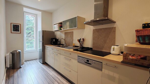 A modern kitchen with a stainless steel range hood, a built-in dishwasher, and a window providing natural light. - Bright apartment with private beach access (Saint-Lunaire)