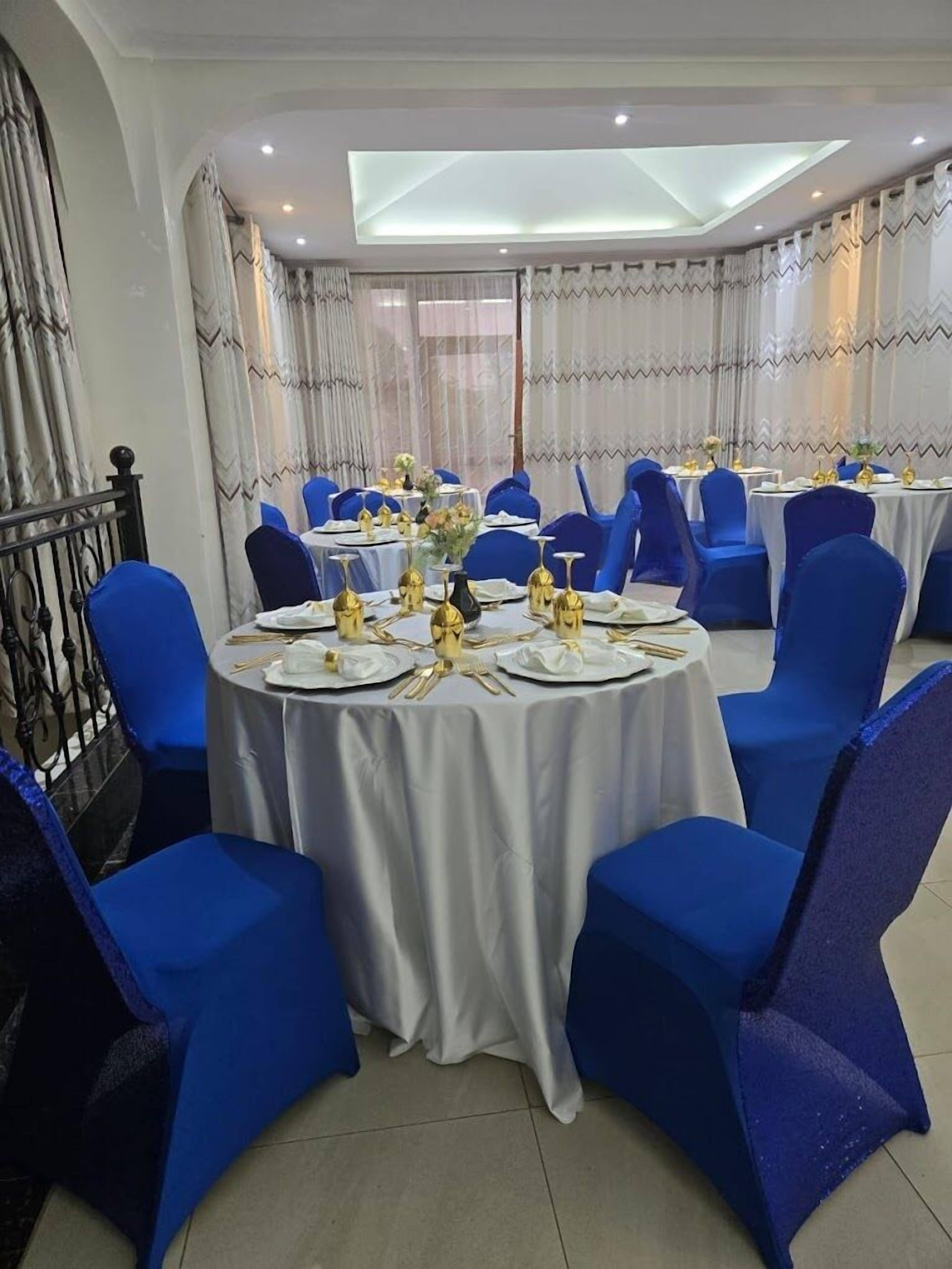 Un salón de banquetes con mesas redondas, sillas azules y manteles blancos.
