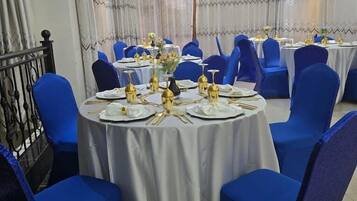 Un salón de banquetes con mesas redondas, sillas azules y manteles blancos.