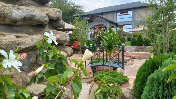 A landscaped garden with a stone wall, a bridge, and a building with large windows. - OLOIRIEN HOTEL & RESORT (Narok)