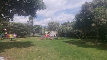 Un parque infantil con toboganes y columpios, rodeado de árboles y césped.