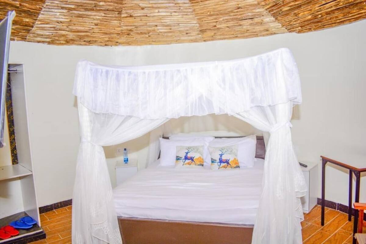 Cama com dossel branco, chão de madeira e prateleira com objeto azul e vermelho.