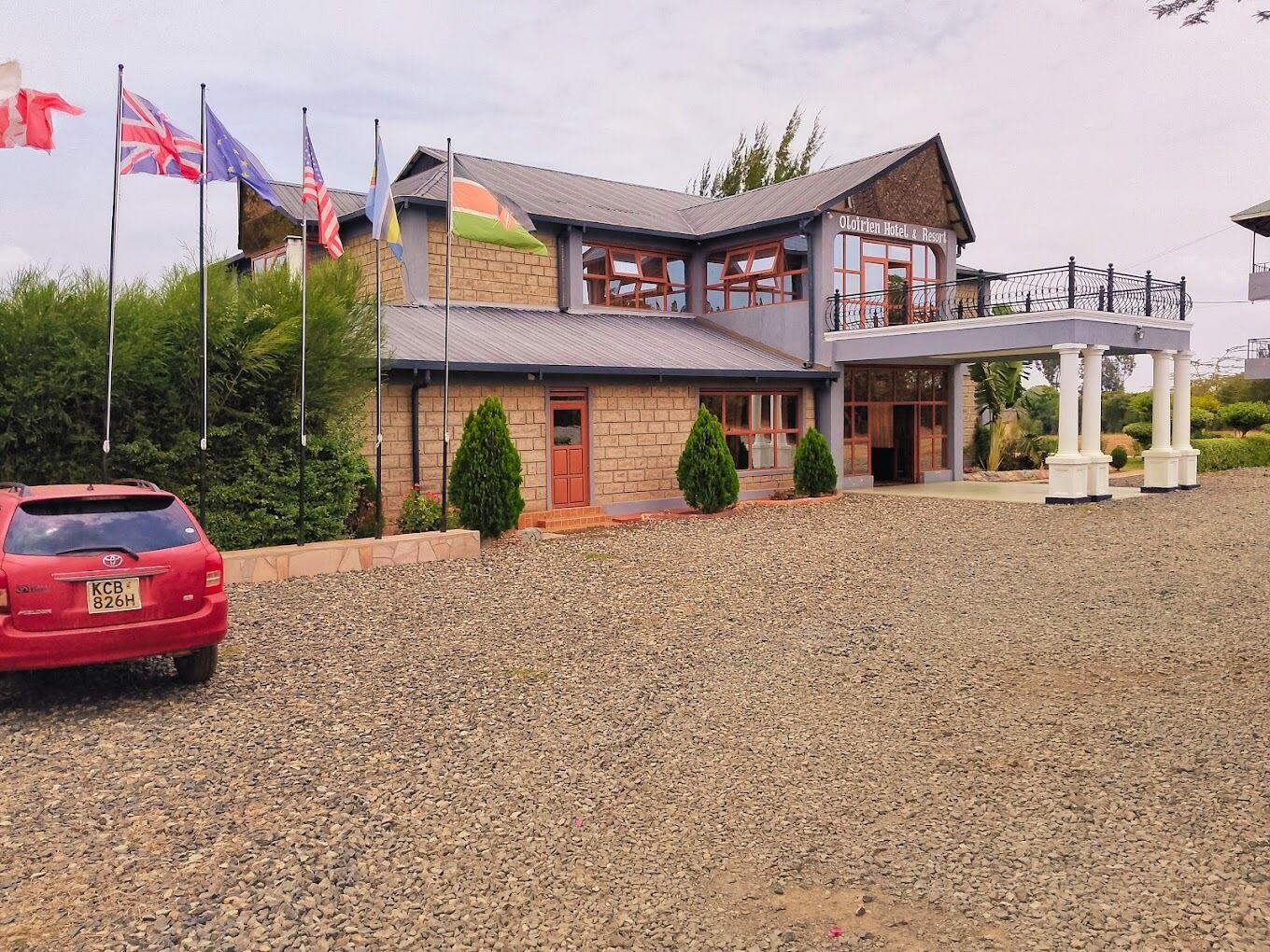 A hotel with a stone facade, a covered outdoor area, and multiple flags.