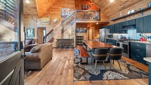 A cozy cabin interior with a wooden staircase, a dining area, and a kitchen.