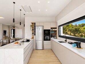 Een moderne keuken met een centraal eiland, inbouwapparatuur en een groot raam met uitzicht op groen.