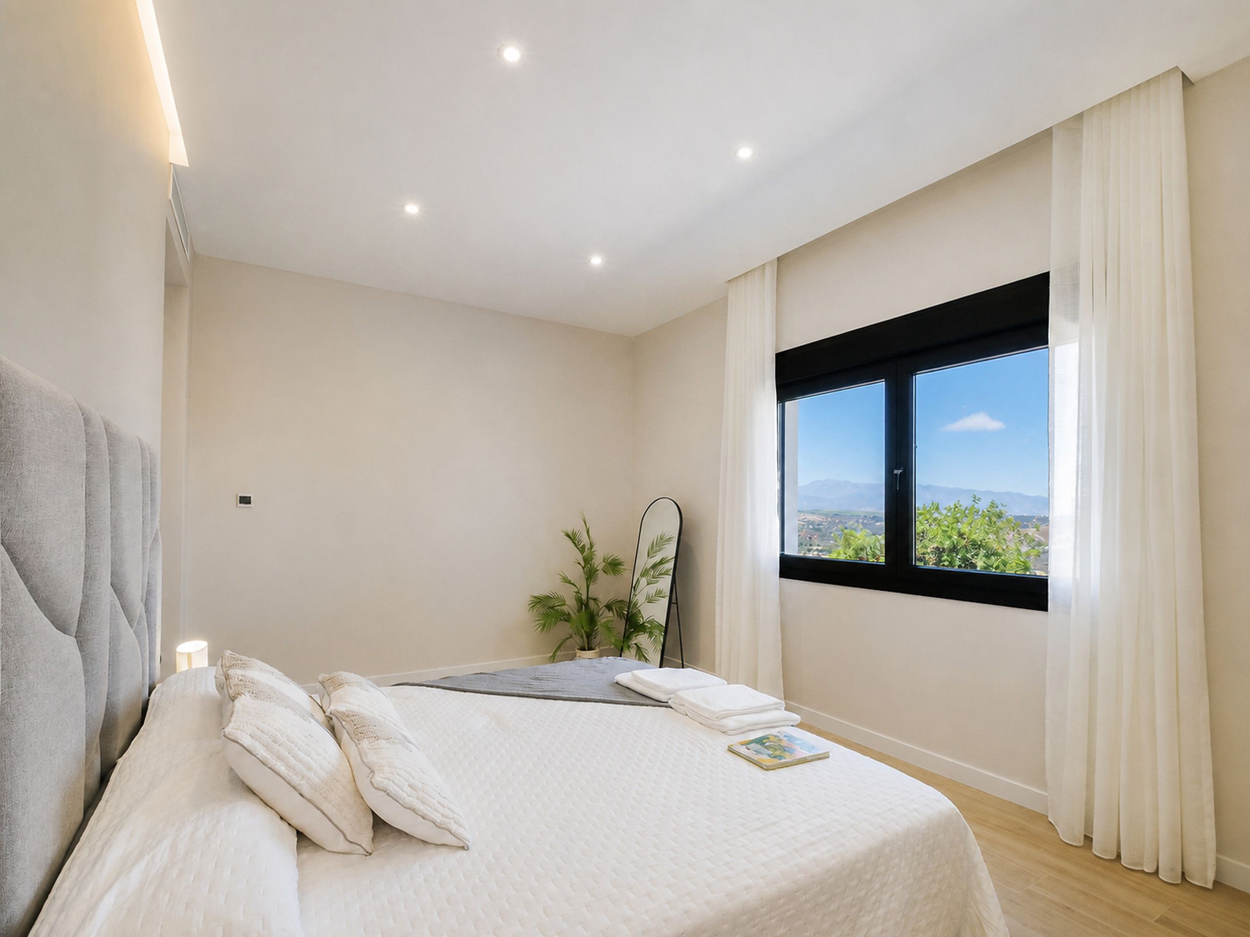 A bedroom with a bed, a window with a view, and a bedside plant.