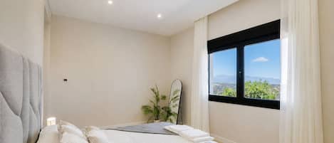 A bedroom with a bed, a window with a view, and a bedside plant.