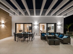 Een terras buiten met een eettafel en stoelen, een zithoek en een plafond met liggende balken.