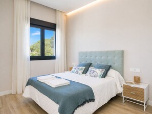 Une chambre à coucher avec un lit, une table de chevet, une fenêtre et une vue sur la verdure.