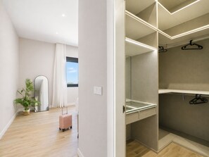 Ein modernes Hotelzimmer mit Holzboden, einem großen Spiegel, einem Blumentopf, einem pinken Koffer und einem begehbaren Kleiderschrank mit Kleiderstange.