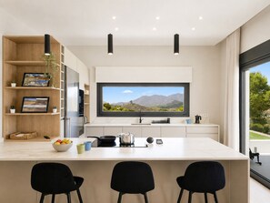 Een moderne keuken met een groot schiereiland, zwarte stoelen, een flatscreen televisie en uitzicht op bergen door een raam.